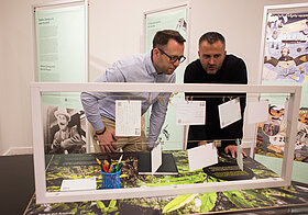 Zwei Männer über eine Schaustation der Ausstellung gebeugt