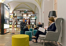 Loungebereich im Literaturmuseum. Besucher*innen sitzen auf gemütlichen Ohrensesseln oder Hockern und lesen in Zeitschriften oder Büchern.
