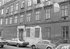 Schwarz-Weiß-Foto einer Fassade eines Zinshauses mit parkenden Autos davor.