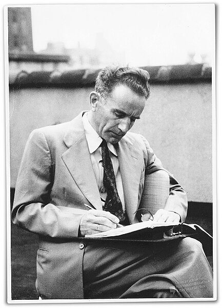 Mann im Anzug sitzt draußen und schreibt in einen Ordner, schwarz-weiß