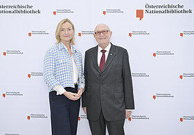 Zwei Personen posieren vor Logowand.