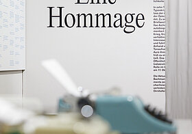 Schreibmaschinen auf einem Tisch, im Hintergrund Text an der Wand.