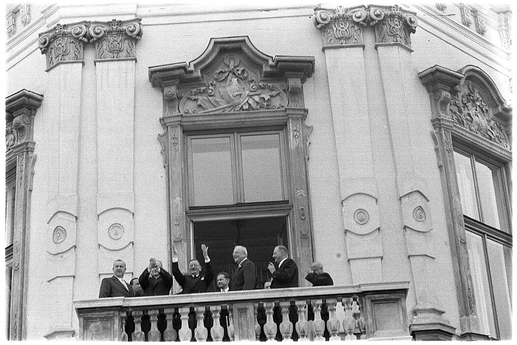 Schwarz-Weiß-Foto eines alten Gebäudes mit einem Balkon mit mehreren Menschen. 