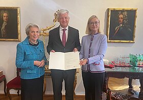 Drei Personen halten eine Urkunde.