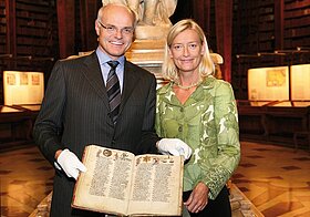 Zwei Personen posieren lächelnd mit aufgeschlagenem Buch. 