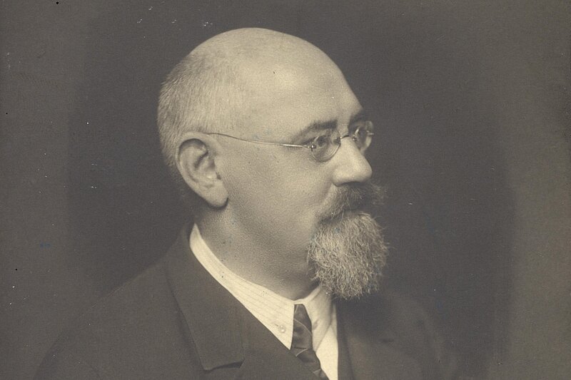 Seitliches Portrait eines Mannes mit Vollbart, Brille und Halbglatze, schwarz-weiß