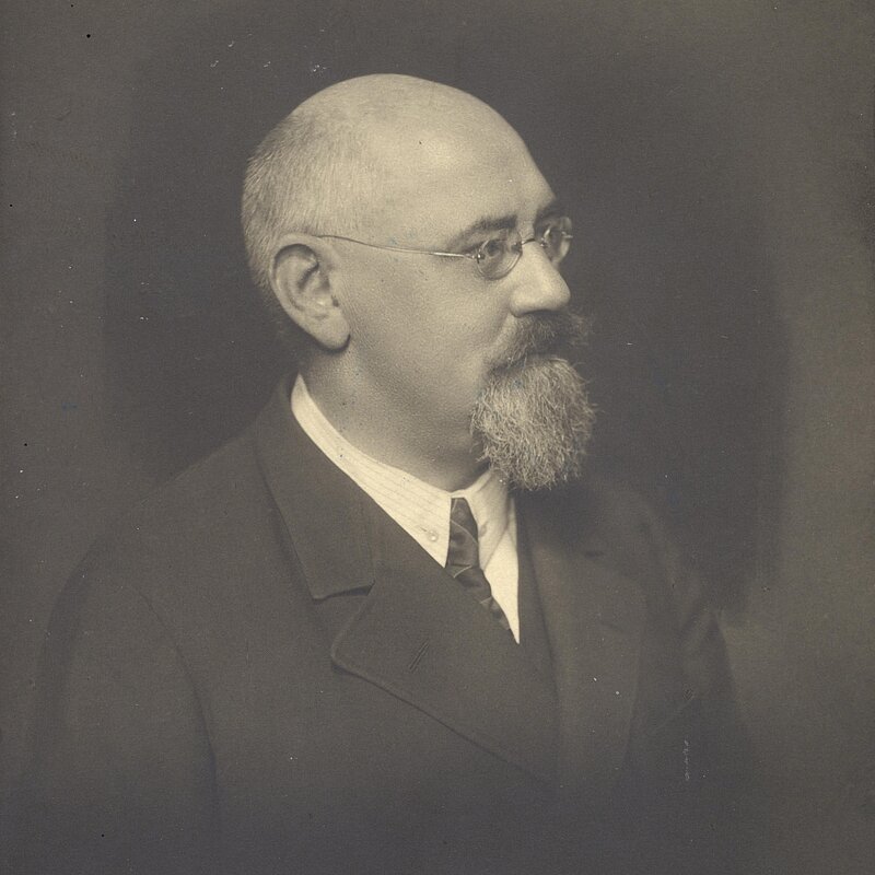 Seitliches Portrait eines Mannes mit Vollbart, Brille und Halbglatze, schwarz-weiß