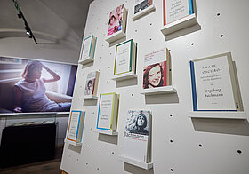 Museumsraum mit einen Foto an der Wand, im Vordergrund ein Regal mit Büchern.