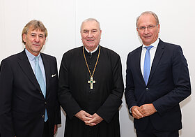 Drei Personen posieren vor weißer Wand.
