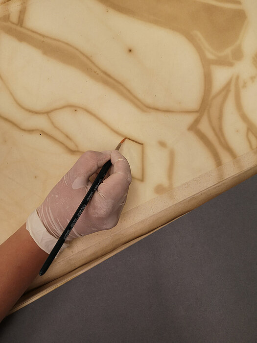 Foto einer Hand die mit Pinsel bräunliche Linien nachzieht.