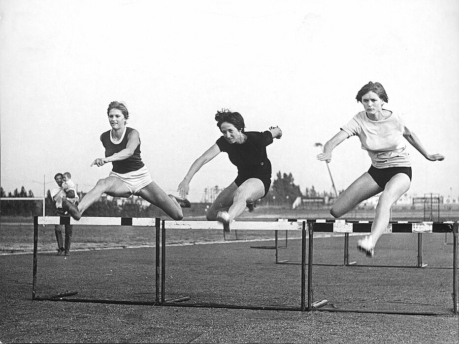 Drei Personen beim Lauf über eine Hürde.