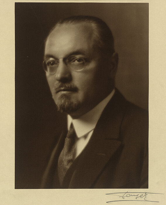 Schwarz-weißes Foto von Person mit Brille und Anzug.