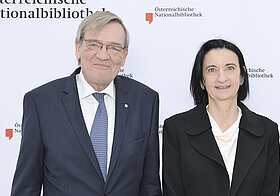 Zwei Personen posieren vor Logowand.