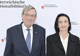 Zwei Personen posieren vor Logowand.