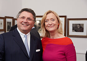 Zwei Personen posieren auf Event vor Wand mit gerahmten Bildern.