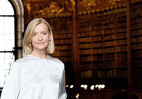 Porträtfoto von einer blonden Frau in weißer Bluse vor Bücherregalen