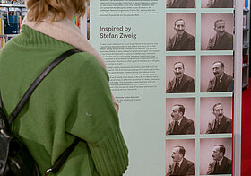 Person betrachtet einen Aufsteller mit türkiser Fläche mit Text, daneben Automatenfotos von Stefan Zweig.