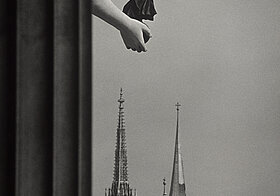 Foto durch Fenster auf Kirchtürme, links die Hand einer Statue.