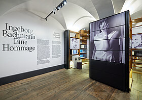 Museumsraum mit Text an der Wand und Regalen mit Fotografien.