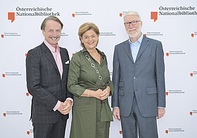 Drei Personen posieren vor einer Logowand.