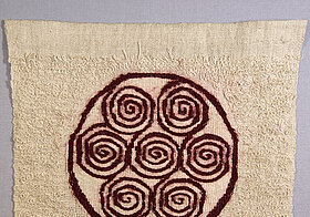 Beiges Stück Stoff mit roten Spiralen in einem Kreis darauf.