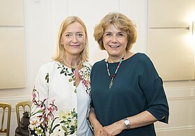 Zwei elegant gekleidete Personen stehen lächelnd nebeneinander. 