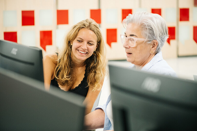 Eine jüngere und eine ältere Person sitzen an einem Computer.