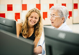 Eine jüngere und eine ältere Person sitzen an einem Computer.