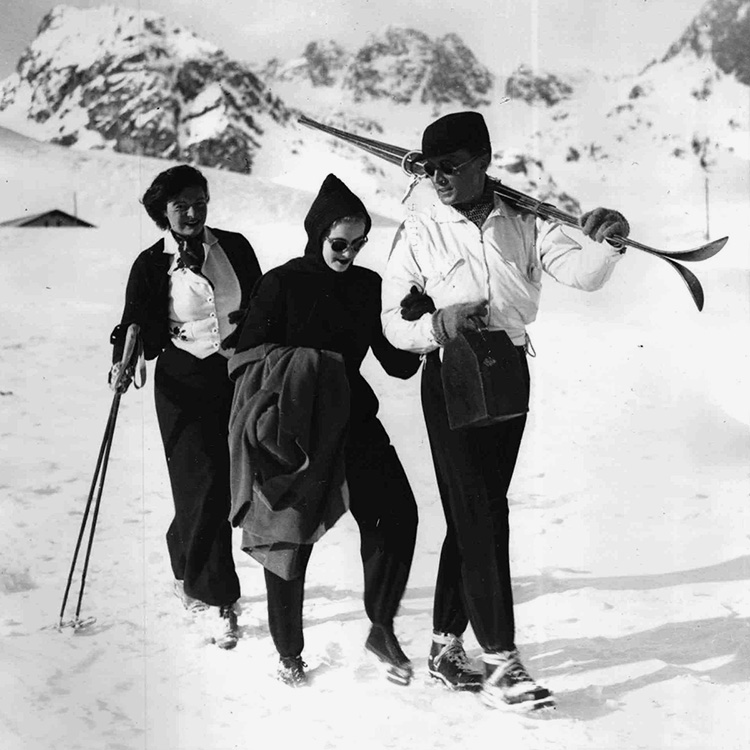 Zwei elegant gekleidete Frauen und ein Mann wandern durch den Schnee