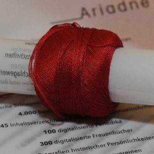 Knäuel aus rotem Faden gewickelt um ein gerolltes Blatt Papier