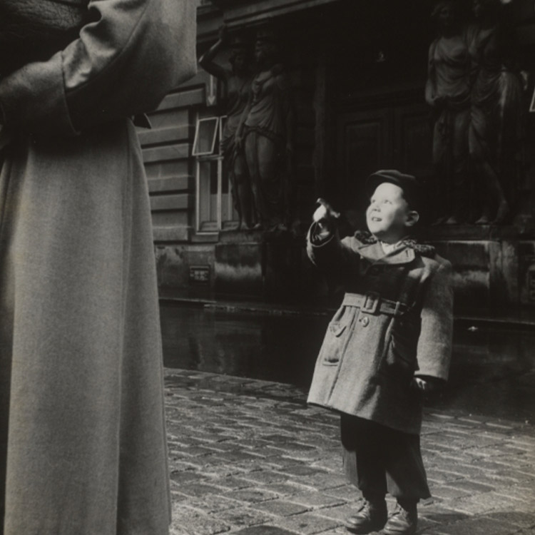 Ein kleiner Junge im Mantel zeigt auf einen Mann, schwarz-weiß